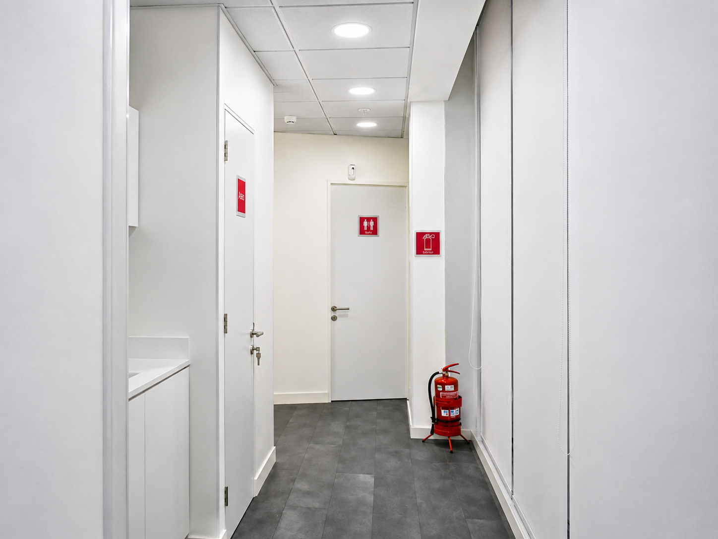 Pasillo de servicio con señalética de baño y extintor en GAES Apoquindo